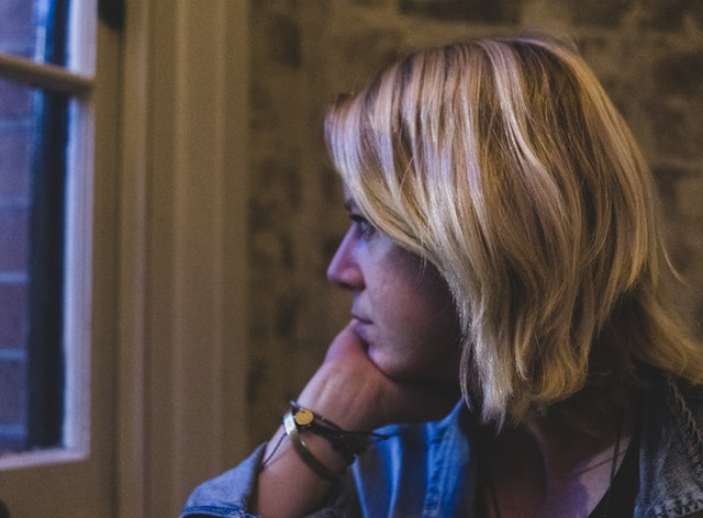 woman putting her head on her hand and thinking while staring out a window