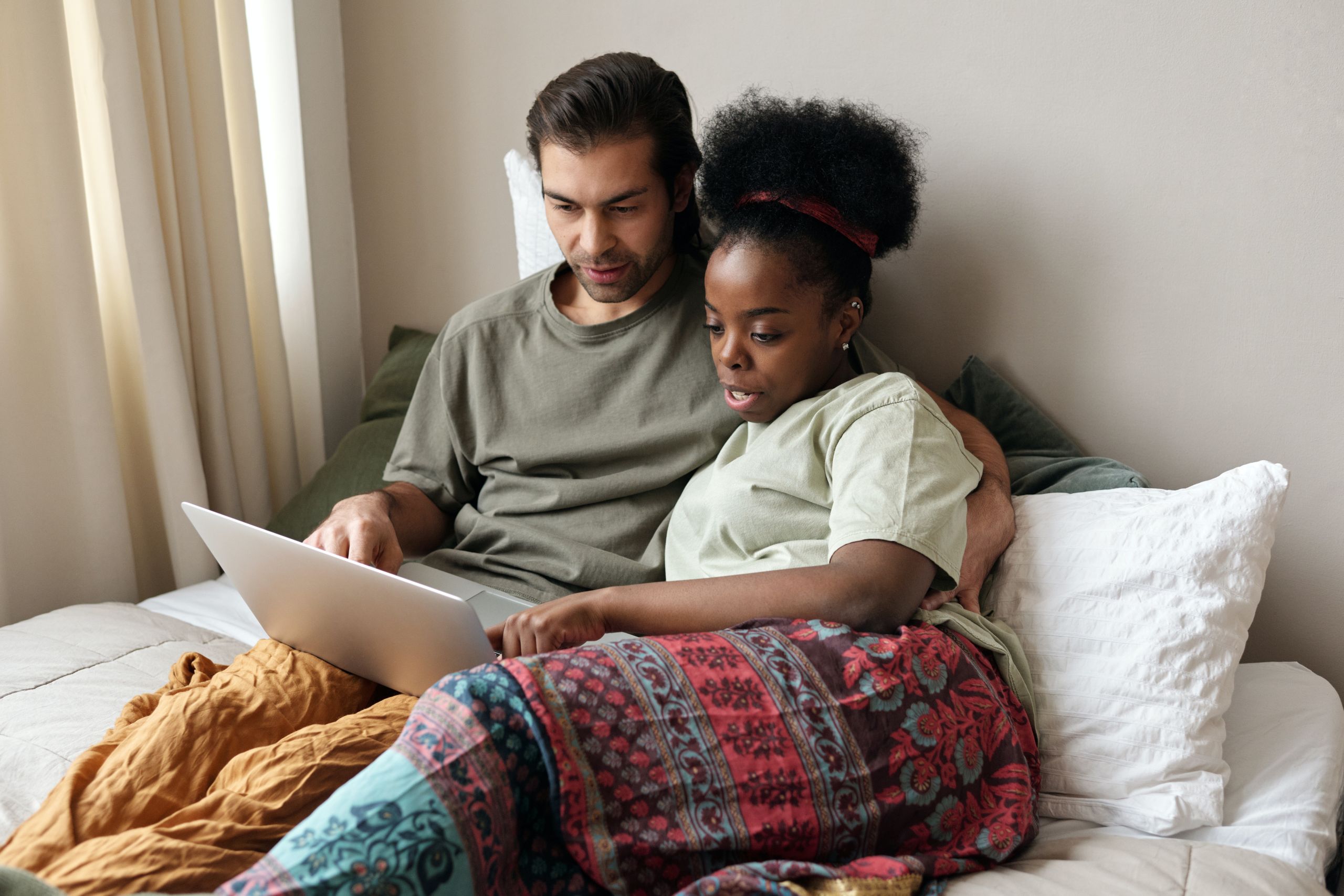 A couple sitting in bed looking at a laptop together